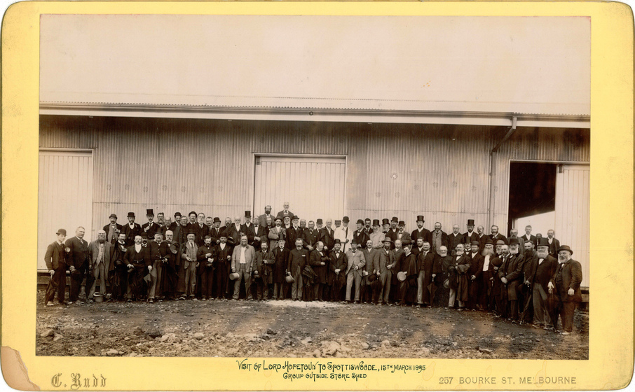 Black and white photograph of large group of men in Victorian dress standing outside a large shed.