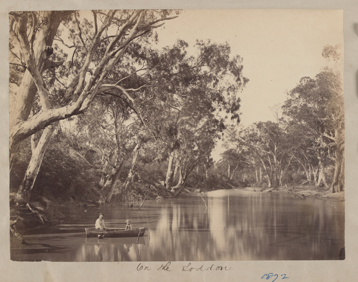 Black and white photograph of man and child in row boat on a river with wooded banks.