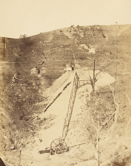 Sepia photograph of bare hillside with tailings heap and winding gear.
