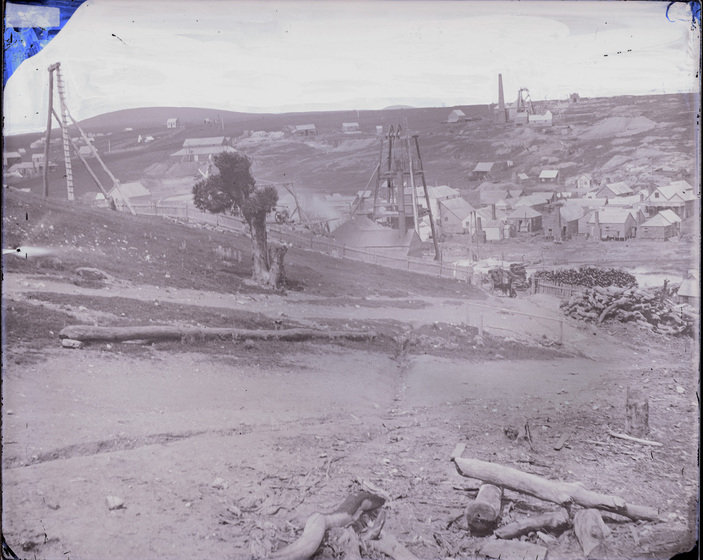 Black and white photograph of shallow denuded valley with cottages and tower for winding gear.