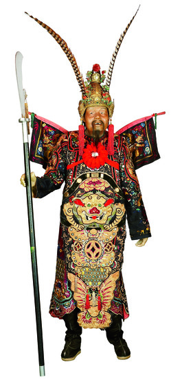 Mannequin holding a staff with blade and dressed in an elaborate headdress and costume embroidered with a large gold dragon and butterfly.