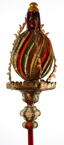 Gilt and red ball with swirling grooves, supported on a pole. 