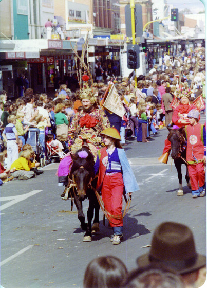 Colour photograph of a bearded man on horseback in an elaborate Chinese costume with a feather headdress in a crowded street.