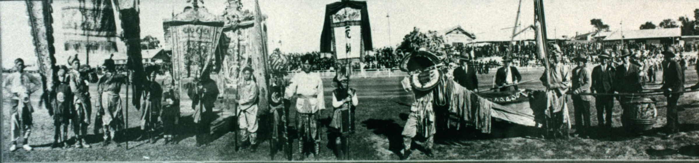 Wide black and white photograph of a row of costumed people some with banners.