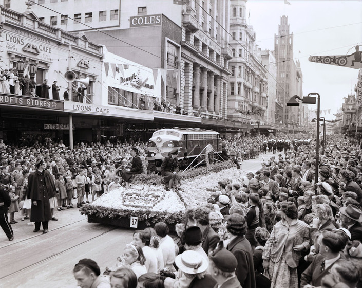 Black and white photograph of a street parade with a large float with a train engine and a large crowd of onlookers.