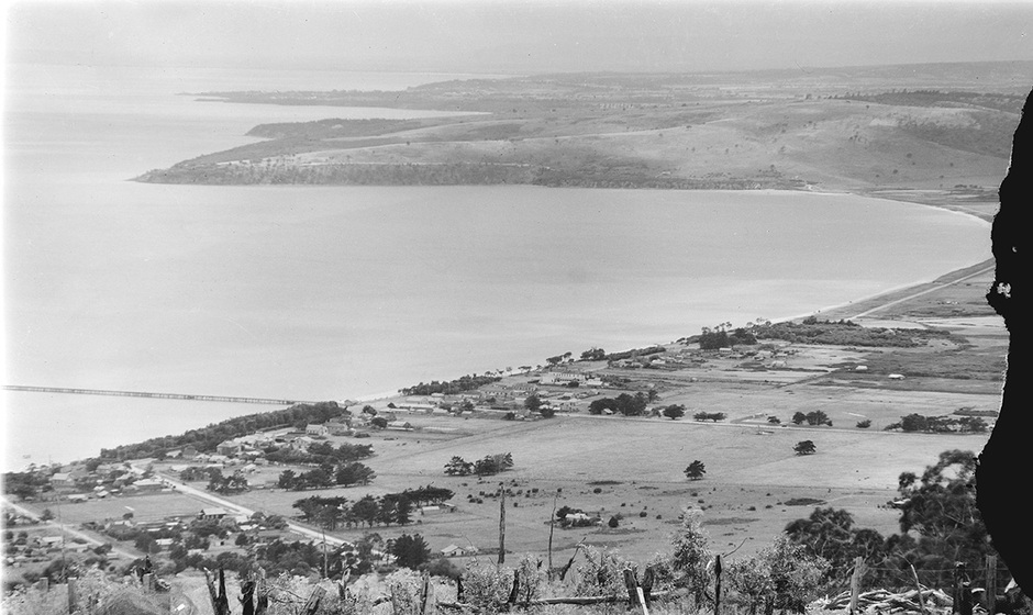 Black and white photographic postcard of a bay with a rural town seen from a high vantage.
