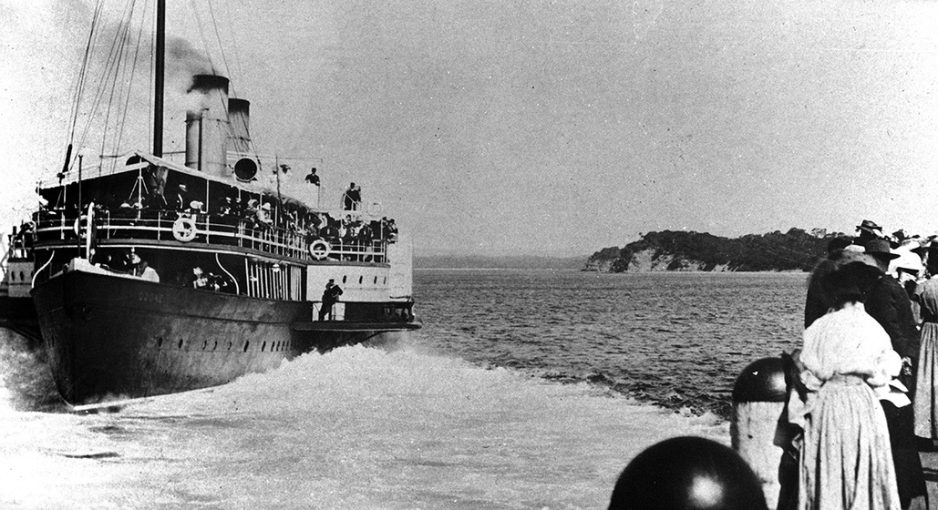 Black and white photographic postcard of a paddle steamer arriving at a pier.