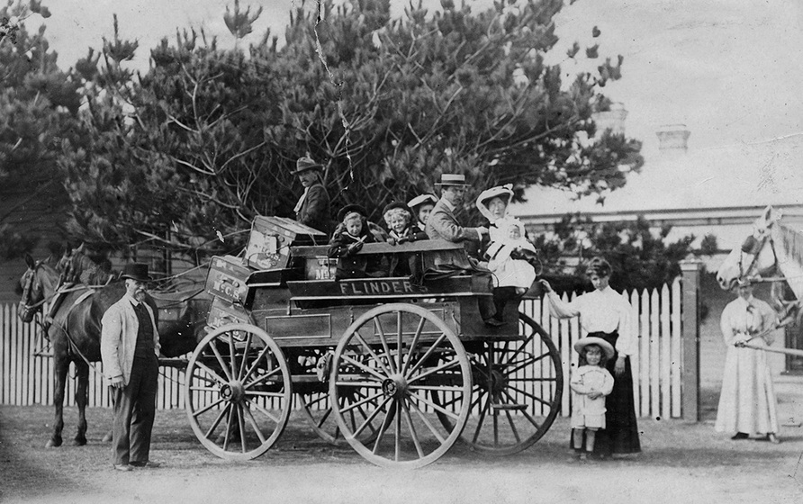 Black and white photograph of men, women, children and luggage on an open horse drawn carriage.