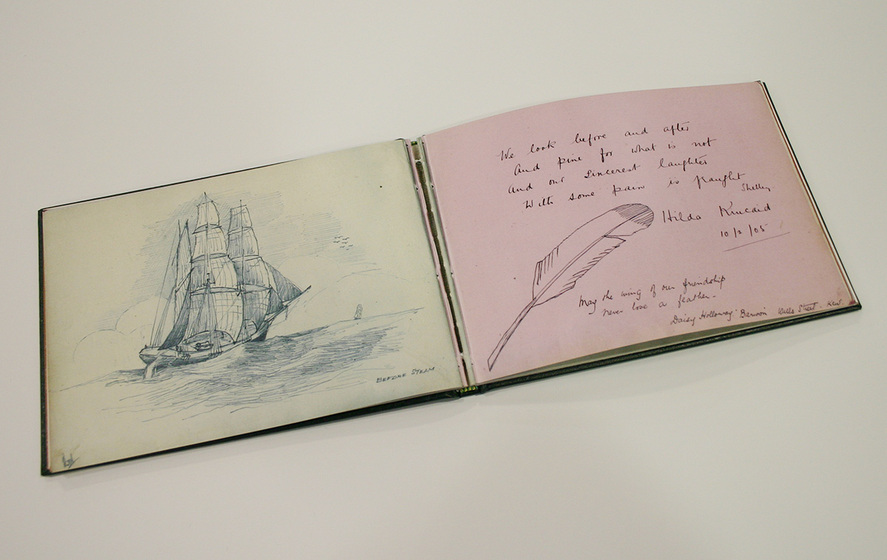 Open double spread of a guest book. Left side white paper with an illustration of a square-rigged sailing ship. Right side pink paper with a handwritten inscription accompanied by an illustration of a feather.