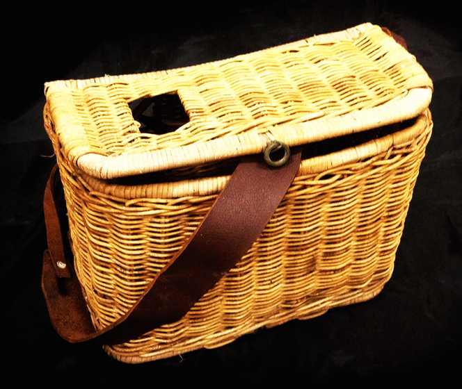 Rectangular wicker fishing basket with square hole in lid and a leather strap.