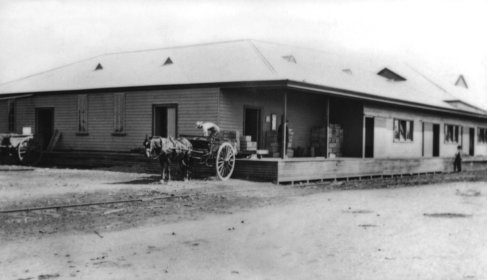 Black and white photograph of a horse drawn cart being loaded at single storey weatherboard building.