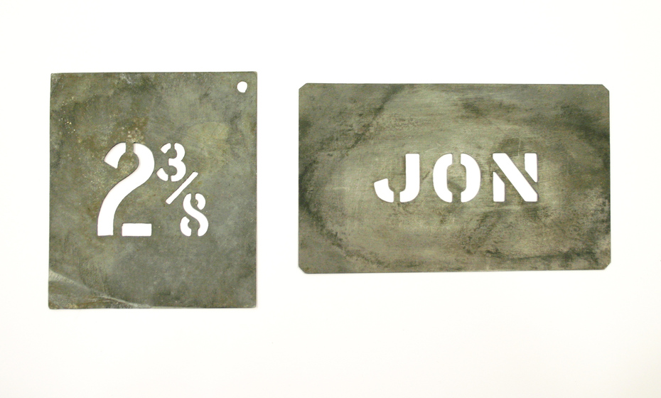 Two metal stencils, one saying '2 3/8' the other saying 'Jon.'