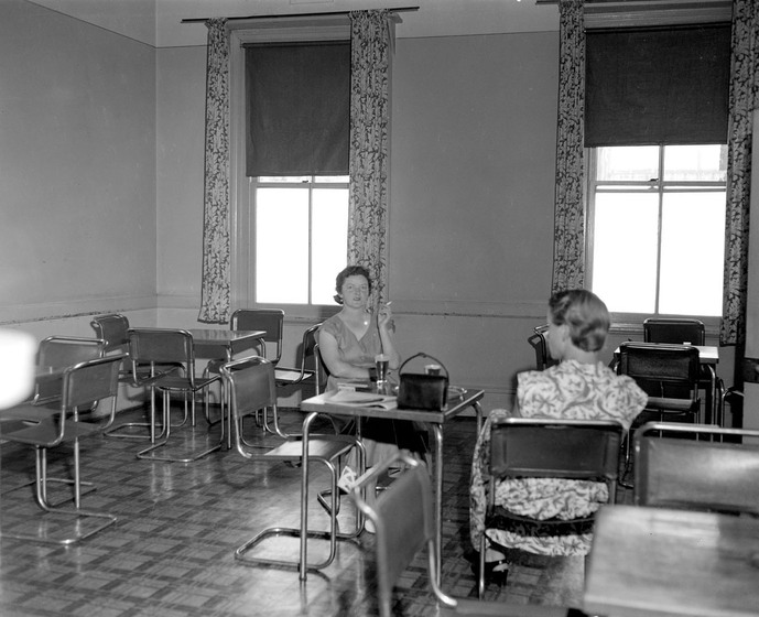 Black and white photograph of two women seated in a hotel bar, one smoking a cigarette.