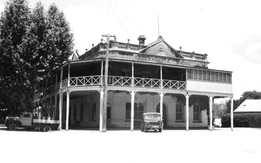 Black and white photograph of a two storey Victorian corner building with wooden verandas on both sides and both floors and the sign, 'Tallangatta Hotel.'