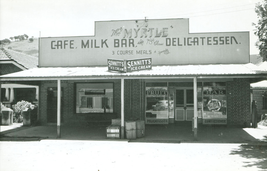 Black and white photograph of a single storey shopfront with a deep veranda. Sign says, 'The Myrtle, Café, Milk Bar and Delicatessen'