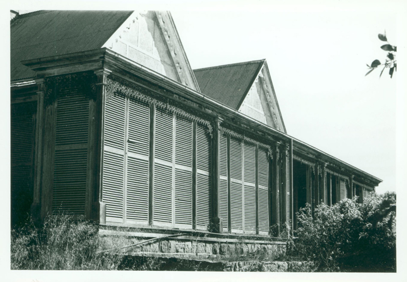 Black and white photograph of a single storey Victorian house with two gables and a shuttered veranda.