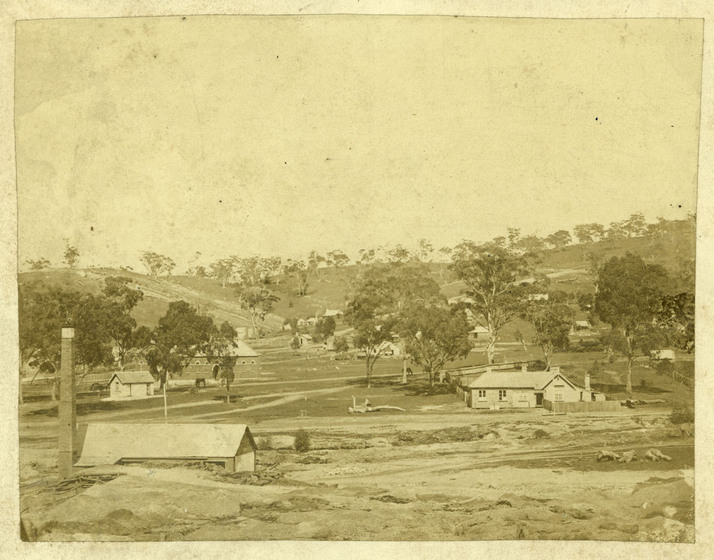 Black and white photograph of a sparse colonial township in a cleared valley.