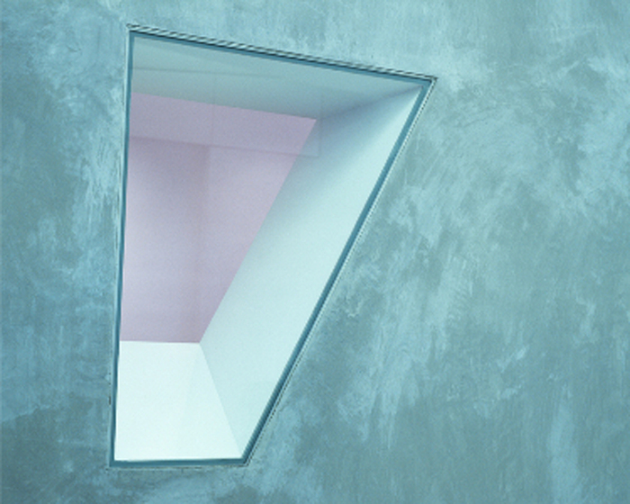 Colour photograph of a wedge-shaped window in a concrete wall taken from the interior.