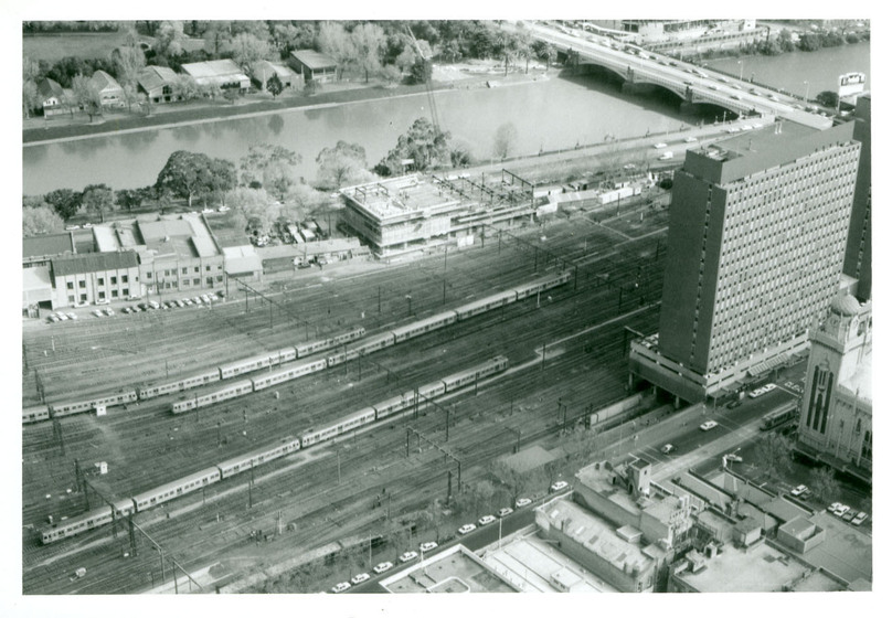 Black and white photograph of an urban railyard beside a river taken from a high vantage point.