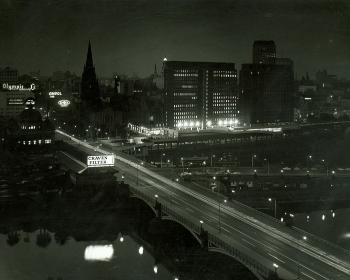 Black and white photograph of a city at night, including a bridge.