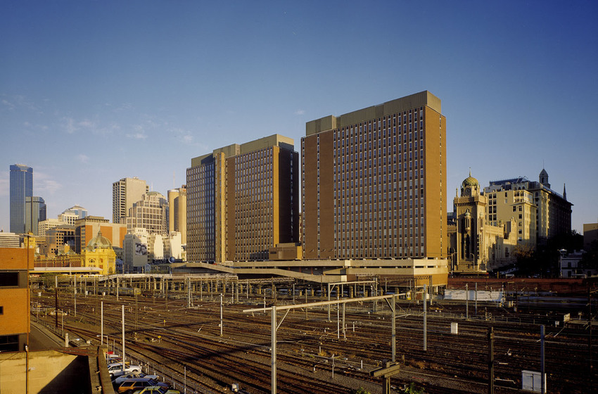 Colour photograph of a pair of brown modernist buildings in a city scape with railyards in front.