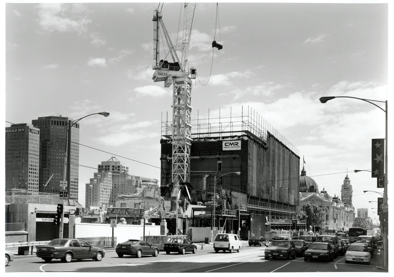 Black and white photograph of a building site in a city with a crane.