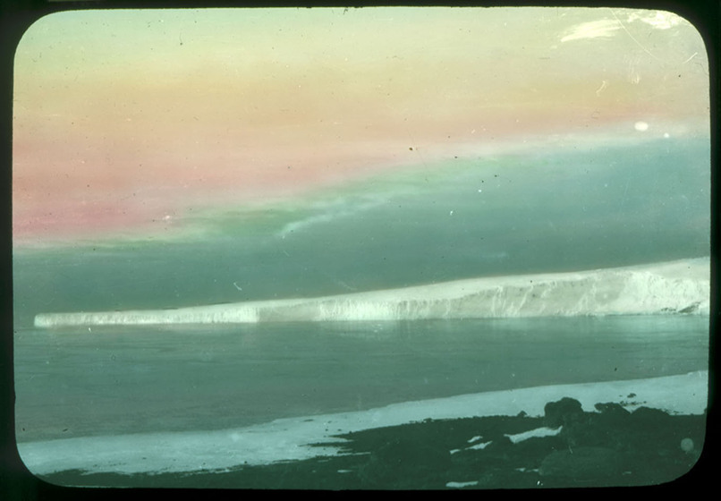Hand-coloured photograph of a glacier descending to the sea.
