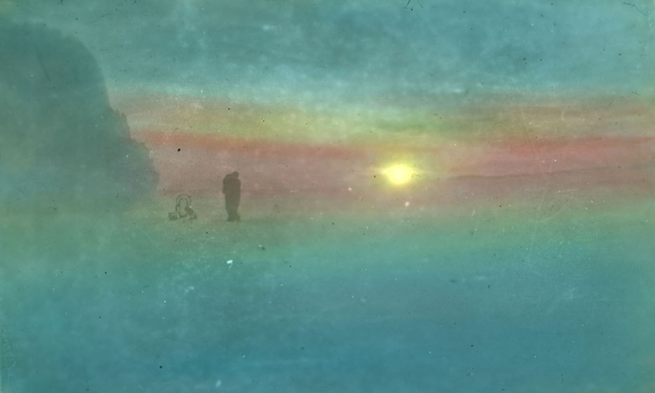 Hand-coloured photograph of the silhouette of a small figure on an icefield with the sun low on the horizon.