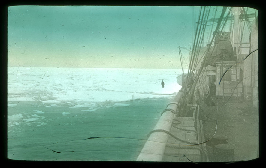 Hand-coloured photograph from the side of sailing vessel looking across icefields with a lone figure.