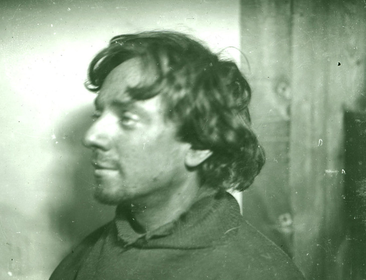 Black and white head and shoulders photo portrait of a man with shaggy hair in profile.