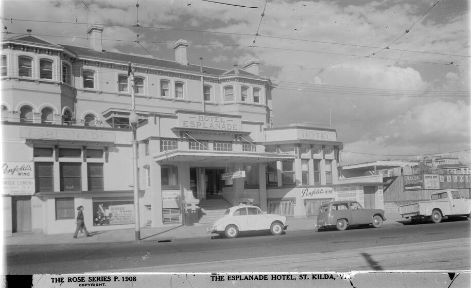 Black and white photograph of three cars parked in front of a three-storey Victorian hotel with modern extensions on the ground level and the sign, 'Esplanade Hotel'.