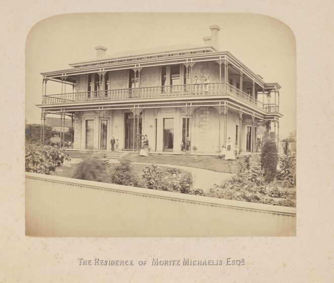 Black and white photograph of seven people standing outside a large two-storey Victorian house with verandahs on both floors, iron lace, bay windows and quoins.