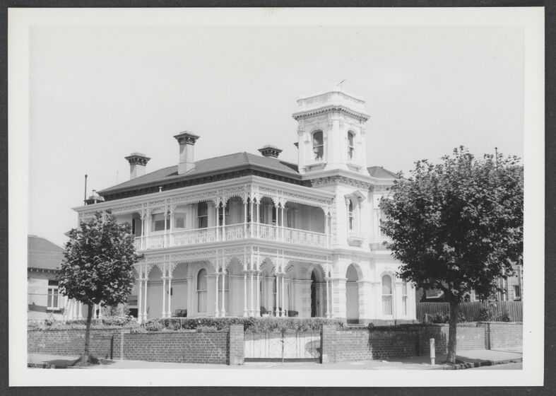 Black and white photograph of a two storey Victorian mansion with verandahs on both floors, a central tower, iron lace and bay windows on a corner block.