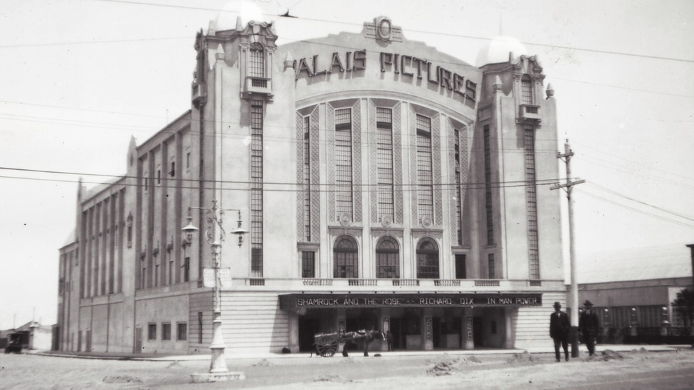 Black and white photograph of the façade of a multi-storey Art Deco cinema with the sign, 'Palais Pictures'.