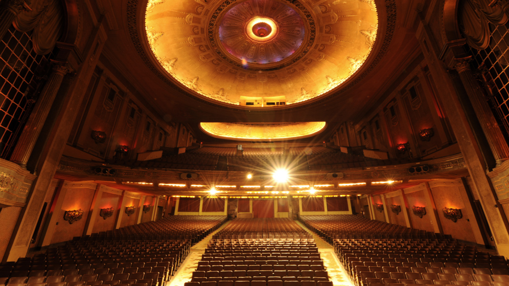 Colour photograph looking from the stage of a theatre into an empty auditorium, an illuminated dome above.