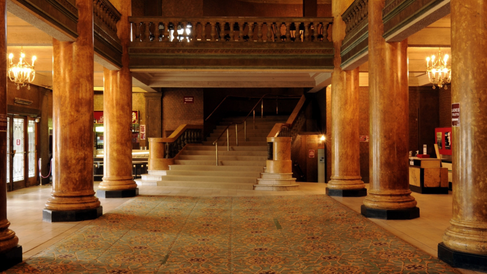 Colour photograph of the foyer of an Art Deco theatre with staircase, columns and gallery.