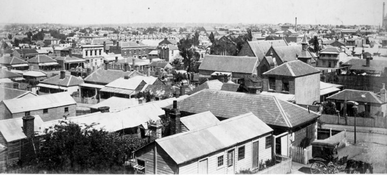 Black and white photograph of an inner city suburb. It is a semi aerial shot showing rooftops of low rise residential weatherboard houses.