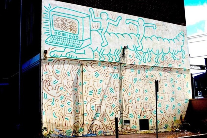 Bright colourful mural on a building wall. The mural is made up of lots of lines and repetitive patterns of human type figures.