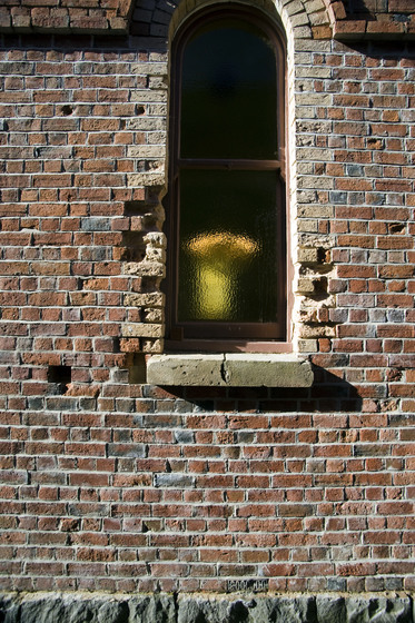 Colour photograph of an arched window in an old brick wall showing decay.