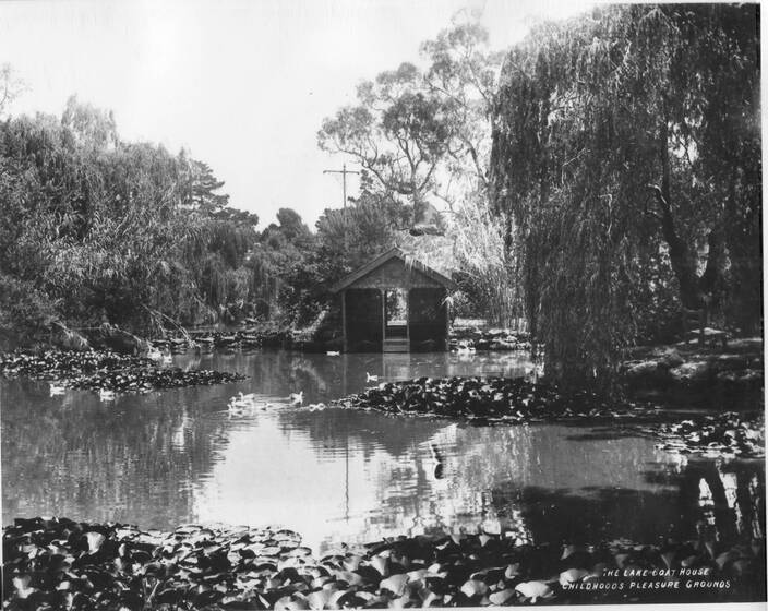Black and white photograph of a boathouse beside a pond surrounded by trees.