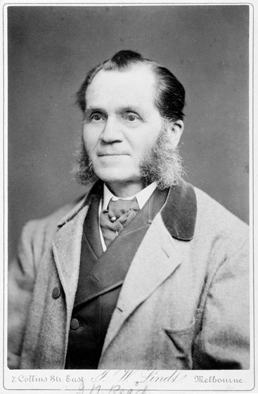 Black and white studio photo portrait of a man with mutton chops in Victorian gentleman's dress with a cravat and tie pin.