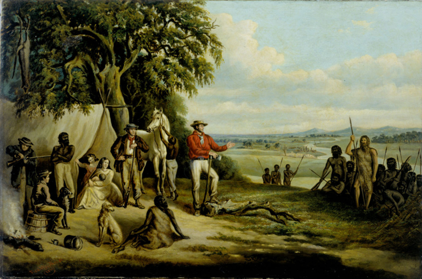 A large tent is set up infront of a gum tree. A group of indigenous men and white men stand and sit around, talking to each other. Some of the men hold spears and some rifles. One figure stands out - a white man who has his hair grown long and is wearing animal skin clothing.