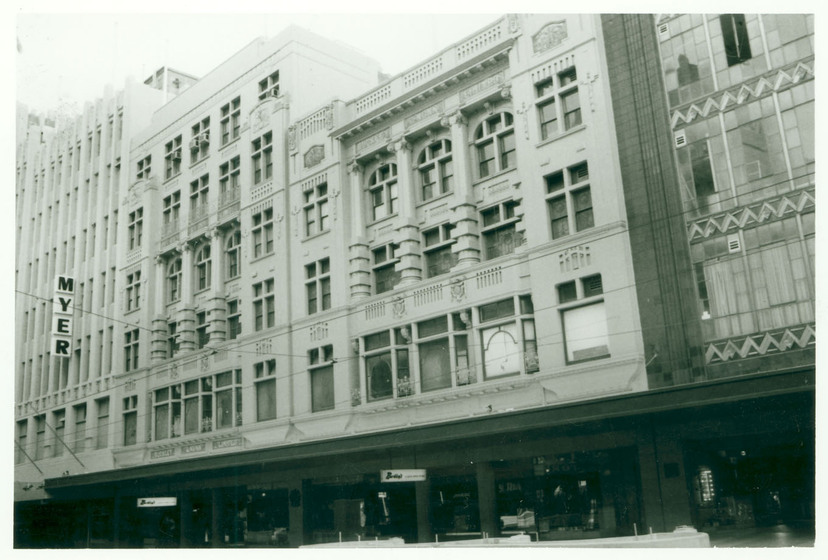 Black and white image of a group of low-rise department store facades. A vertical MYER sign can be seen on the front of one of the buildings.