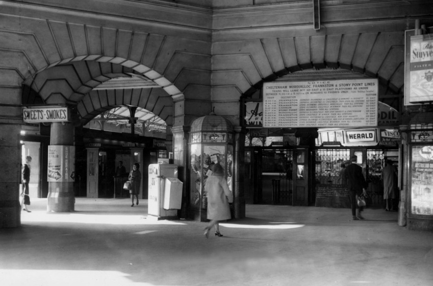 The inside of the station entrance, with lots of archways and columns. A handful of commuters walk through the open space.