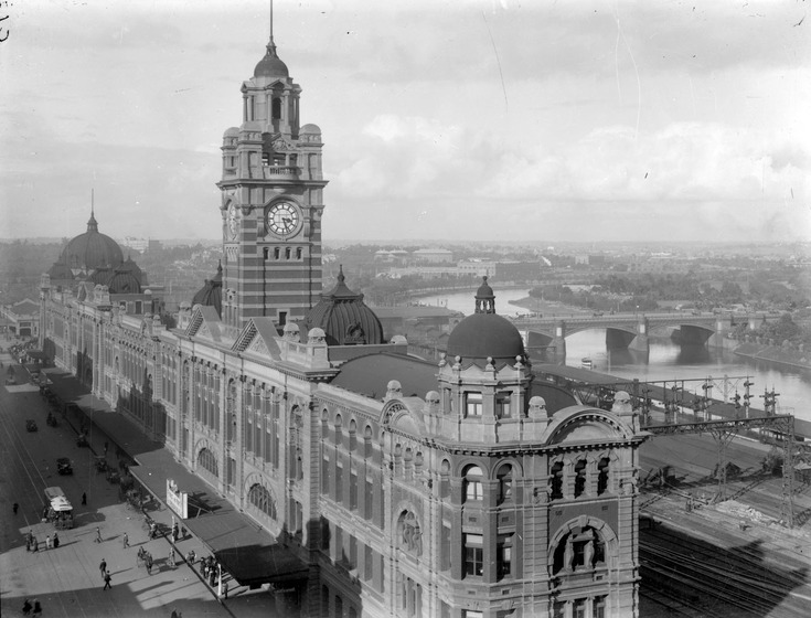 Photograph taken from a high vantage point, looking back towards Flinders Street Station. The clock tower can be seen in the centre of the building and in the distance is the domed roof. To the right of the station, the river and Princes Street Bridge can be seen.