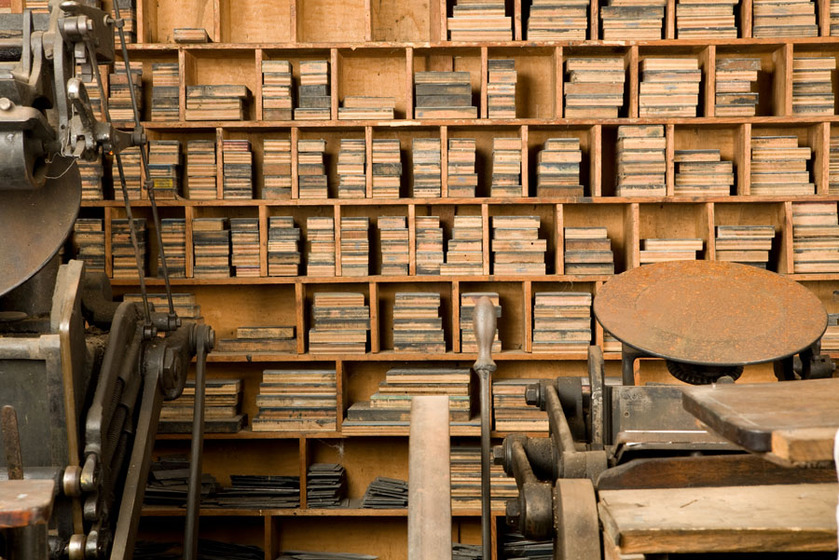 A wooden shelf lines with lots of small small wooden boxes. In each box is a stack of wooden loose type plates.