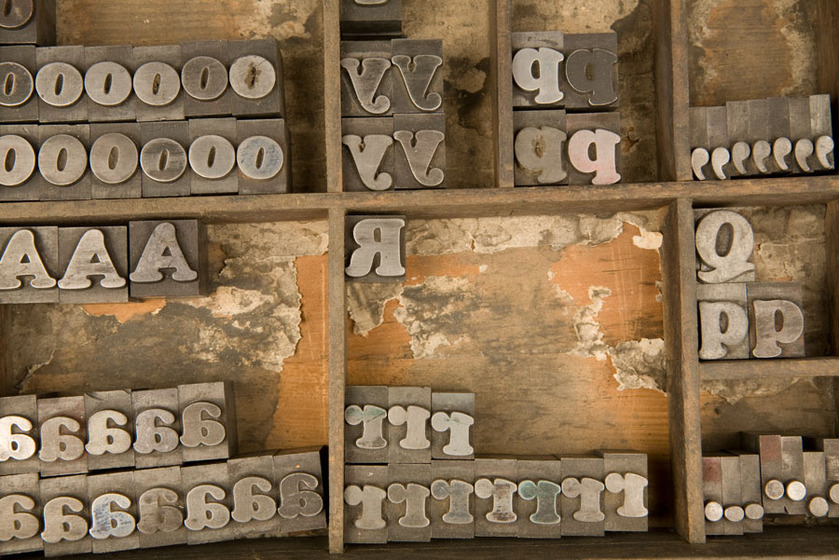 A wooden tray with six sections. In each section is a selection of loose type with letters and punctuation symbols on them.