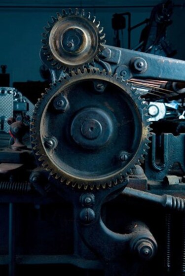 A close up of a piece of metal machinery. The machine has lots of wheels, cogs and handles to turn the parts.