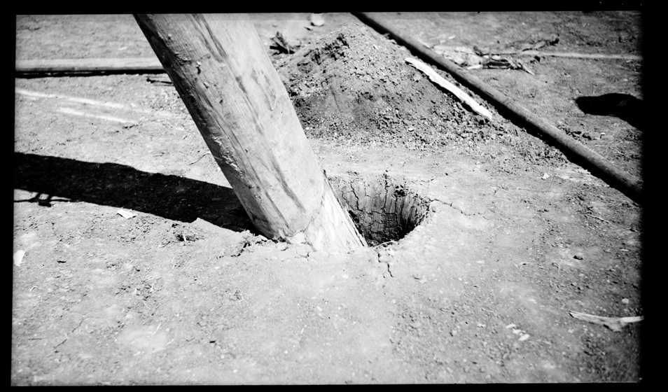 A large wooden pole sits in a hole in the ground - it is on a slight angle.