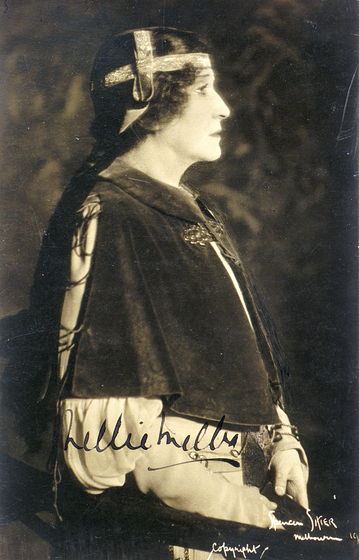 Black and white profile photograph of a woman dressed in costume. She is wearing a bolero clasped together below the neck, and a head piece made of ribbons.